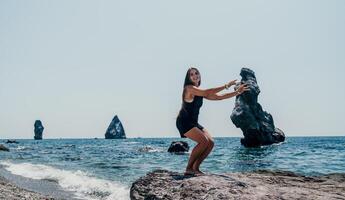 kvinna sommar resa hav. Lycklig turist i hatt njut av tar bild utomhus för minnen. kvinna resande Framställ på de strand på hav omgiven förbi vulkanisk berg, delning resa äventyr resa foto