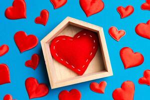 stänga upp av röd hjärta i en trä- hus dekorerad med små hjärtan på färgrik bakgrund. hjärtans dag. Hem ljuv Hem begrepp foto