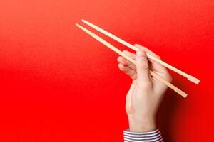 Pojkar hand som visar ätpinnar på röd bakgrund. asiatisk kök begrepp med tömma Plats för din design foto