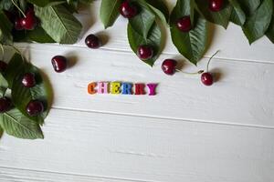 de gren med mogen körsbär och Flerfärgad brev på en vit trä- tabell. foto