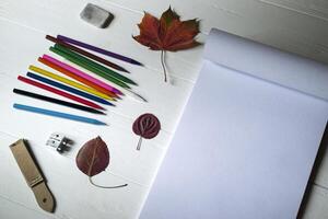 tömma skiss vaddera, färgrik pennor, Övrig Utrustning för teckning och fallen blad på de vit trä- skrivbordet. konst bakgrund med plats för text. foto