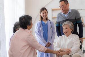 asiatisk ung sjuksköterska Stöd par senior äldre man och kvinna i en rullstol. äldre mogna och en grupp av senior vänner levande i de sjukhus. umgänge av pensionerad människor. foto