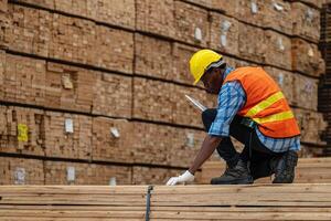 afrikansk arbetare man teknik gående och inspekterande med arbetssätt svit klänning och hand handske i timmer trä lager. begrepp av smart industri arbetstagare fungerar. trä fabriker producera trä gom. foto