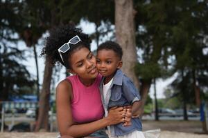 blandad lopp afrikansk och asiatisk mor och pojke är spelar på de utomhus- område. leende Lycklig familj ha roligt löpning på de strand. porträtt av mamma och unge livsstil med en unik frisyr. foto