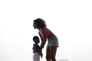 blandad lopp afrikansk och asiatisk mor och pojke är spelar på de utomhus- område. leende Lycklig familj ha roligt löpning på de strand. porträtt av mamma och unge livsstil med en unik frisyr. foto