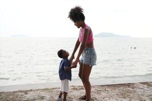 blandad lopp afrikansk och asiatisk mor och pojke är spelar på de utomhus- område. leende Lycklig familj ha roligt löpning på de strand. porträtt av mamma och unge livsstil med en unik frisyr. foto