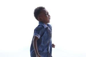 blandad lopp afrikansk och asiatisk pojke är spelar på de utomhus- område. leende Lycklig pojke har roligt löpning på de strand. porträtt av pojke livsstil med en unik frisyr. foto