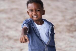 blandad lopp afrikansk och asiatisk pojke är spelar på de utomhus- område. leende Lycklig pojke har roligt löpning på de strand. porträtt av pojke livsstil med en unik frisyr. foto