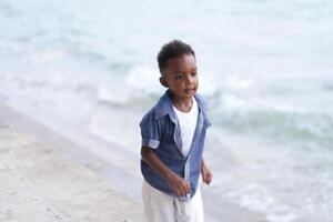 blandad lopp afrikansk och asiatisk pojke är spelar på de utomhus- område. leende Lycklig pojke har roligt löpning på de strand. porträtt av pojke livsstil med en unik frisyr. foto