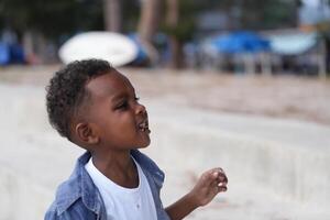 blandad lopp afrikansk och asiatisk pojke är spelar på de utomhus- område. leende Lycklig pojke har roligt löpning på de strand. porträtt av pojke livsstil med en unik frisyr. foto