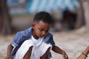 blandad lopp afrikansk och asiatisk pojke är spelar på de utomhus- område. leende Lycklig pojke har roligt löpning på de strand. porträtt av pojke livsstil med en unik frisyr. foto