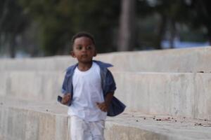 blandad lopp afrikansk och asiatisk pojke är spelar på de utomhus- område. leende Lycklig pojke har roligt löpning på de strand. porträtt av pojke livsstil med en unik frisyr. foto