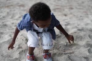 blandad lopp afrikansk och asiatisk pojke är spelar på de utomhus- område. leende Lycklig pojke har roligt löpning på de strand. porträtt av pojke livsstil med en unik frisyr. foto