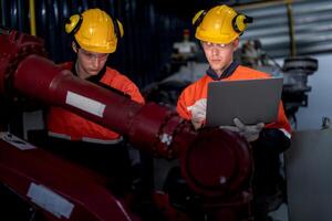 grupp av manlig ingenjör arbetare underhåll automatisk robot ärm maskin i en mörk rum fabrik. arbetstagare kontroll och reparation automatisk robot hand maskin. arbetstagare bär säkerhet glasögon och hjälm. foto