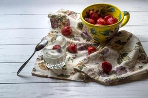 en råna av mogen jordgubbar och glas av grädde på en vit trä- tabell. de friska mat. foto