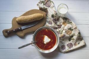 röd soppa, bröd och sur grädde på en vit trä- tabell. borscht - en traditionell maträtt av ryska kök. foto