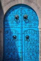 en blå dörr med svart dubbar och sten prydnad på dörröppning i tunisien foto