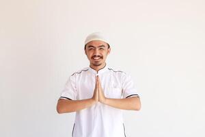 leende ung asiatisk muslim man i baju koko stående med gestikulerar eid mubarak hälsning foto