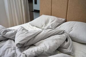 skrynkliga säng med kuddar, filt och skrynkliga ark i sovrum foto