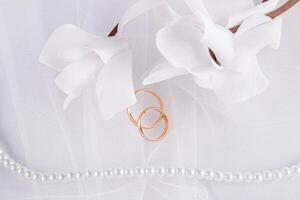 delikat bröllop arrangemang med två bröllop guld ringar på en vit slöja bakgrund med pärla pärlor och blommor. vykort. inbjudan. omslag foto