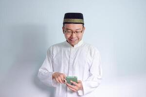 asiatisk muslim man bär glasögon och vit trasa pekande telefon utgör för Ramadhan och eid al fitr. isolerat vit bakgrund foto