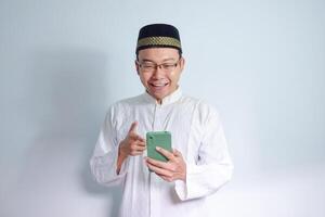 asiatisk muslim man bär glasögon och vit trasa pekande telefon utgör för Ramadhan och eid al fitr. isolerat vit bakgrund foto