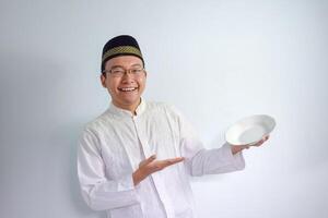 asiatisk muslim man bär glasögon och vit trasa pekande tömma tallrik för fasta ramadhan. isolerat vit bakgrund foto
