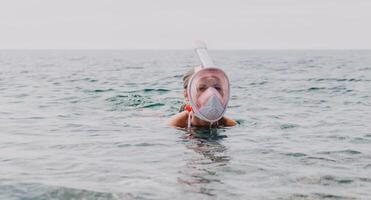 ung Lycklig kvinna i vit bikini och bär rosa mask får redo för hav snorkling. positiv leende kvinna avkopplande och njuter vatten aktiviteter med familj sommar resa högtider semester på hav. foto