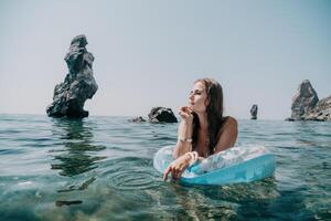 kvinna sommar hav. Lycklig kvinna simning med uppblåsbar munk på de strand i sommar solig dag, omgiven förbi vulkanisk berg. sommar semester begrepp. foto