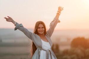 Lycklig kvinna stående med henne tillbaka på de solnedgång i natur i sommar med öppen händer. romantisk skön brud i vit boho klänning Framställ med bergen på solnedgång foto