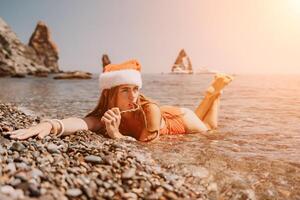 kvinna resa hav. Lycklig turist njut av tar bild på de strand för minnen. kvinna resande i santa hatt utseende på kamera på de hav bukt, delning resa äventyr resa foto