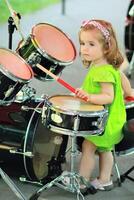ett år gammal söt flicka i en grön romper inlärning på vilket sätt till spela trummor utomhus foto