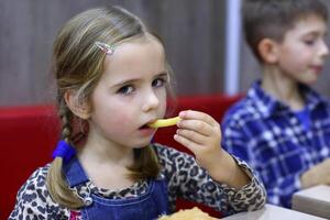 porträtt av en caucasian fyra år gammal flicka äter franska frites i en Kafé foto