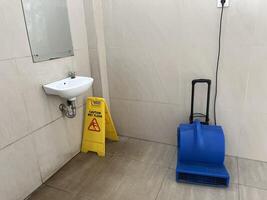 varning våt golv gul varning styrelse under de handfat med blå golv torktumlare i offentlig toalett foto