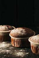 choklad muffins med pulveriserad socker på en svart bakgrund. fortfarande liv stänga upp. mörk lynnig. mat Foto. foto
