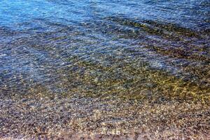 bakgrund av de vatten av sjö Traunsee i de kust område. färgrik textur av stenar under vatten. foto