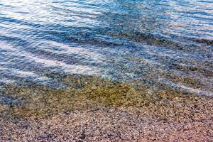 bakgrund av de vatten av sjö Traunsee i de kust område. färgrik textur av stenar under vatten. foto