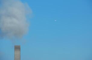 rök från en skorsten och ett flygplan mot en bakgrund av blå himmel på en solig dag. foto