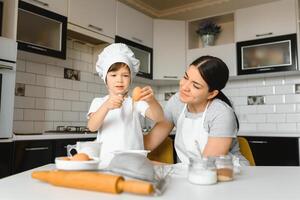 en ung och skön mamma är framställning mat på Hem i de kök, längs med henne liten son foto