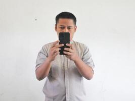 vuxen asiatisk man textning på hans mobil telefon med arg allvarlig uttryck foto