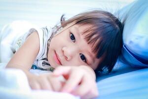 en liten asiatisk flicka är sjuk med en feber. hon var liggande på de säng i de sjukhus undersökning rum. begrepp av barns sjukdom, viral infektion, medicinsk tjänster foto