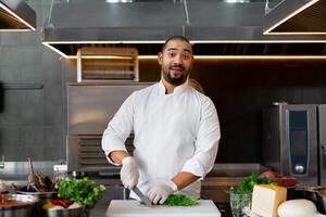 stilig ung afrikansk kock stående i professionell kök i restaurang framställning en måltid av kött och ost grönsaker. foto