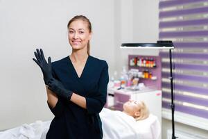kosmetologi skåp klient lögner på soffa. kosmetolog står och sätter svart skyddande handskar på hans hand och ler. foto