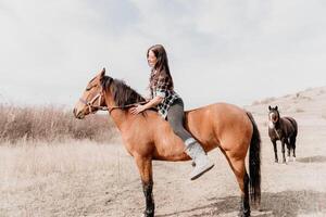 ung Lycklig kvinna i hatt med henne häst i kväll solnedgång ljus. utomhus- fotografi med mode modell flicka. livsstil humör. begrepp av utomhus- ridning, sporter och rekreation. foto