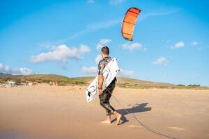 porträtt Vinka kitesurfer gående strand med hans styrelse och drake foto