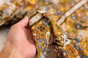 en hand innehav traditionell indonesiska tyg, nämligen batik trasa. indonesien med elegant klassisk motiv foto