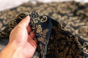 en hand innehav traditionell indonesiska tyg, nämligen batik trasa. indonesien med elegant klassisk motiv foto