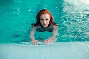 skön ung rödhårig caucasian flicka simmar i de inomhus- simning slå samman. friska livsstil. foto