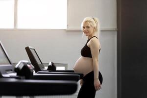 gravid kvinna Träning löpband maskin i Gym konditionsträning övningar på löpning simulator foto