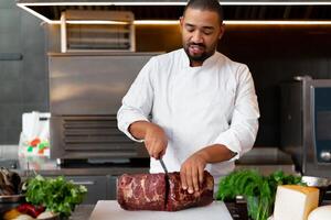 stilig ung afrikansk kock stående i professionell kök i restaurang framställning en måltid av kött och ost grönsaker. foto